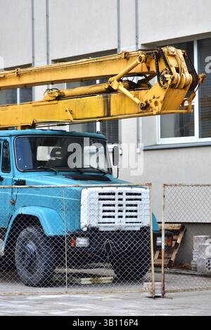 Old school russian vintage man lifter crane truck service standing near school building. Soviet heritage old rusty crane truck. Stock Photo