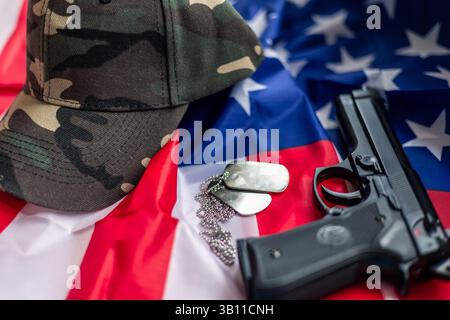Military service concept with camouflage cap, handgun and dog tags lying on United States flag, celebrating memorial day, veterans day or independence Stock Photo