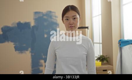 Woman standing in newly painted living room, with blue walls, looking contemplatively into the camera, suggesting home renovation or decoration, showc Stock Photo