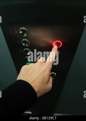 Close-up of a hand pressing an elevator button highlighted with a red-lit indicator Stock Photo