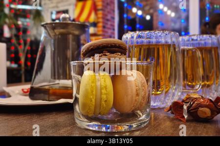 Closeup of a glass with tasty macarons cookies and tea cups on the table inside a fancy and cozy cafe Stock Photo