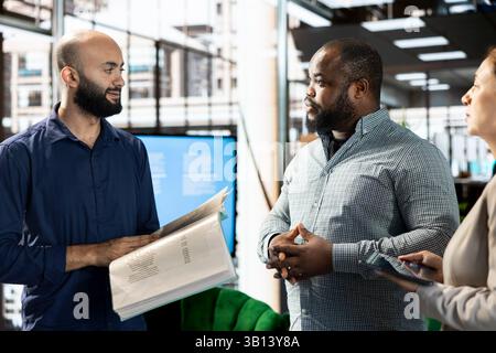 Middle Eastern businessman talking with coworker in startup company, looking at financial business documents. Diverse team of office clerks checking accounting figures in paperwork Stock Photo