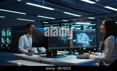 Team of engineers using AI tech on computer to do checkup in server room. Data center workers using artificial intelligence technology to process datasets for training, camera B Stock Photo