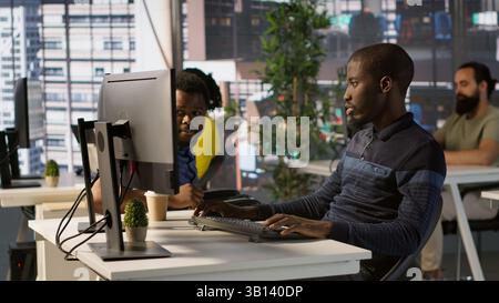 Happy coworker in wheelchair bumping fists with programmer testing machine learning technology. Person with disability saluting colleague in inclusive office, doing friendly gesture, camera A Stock Photo