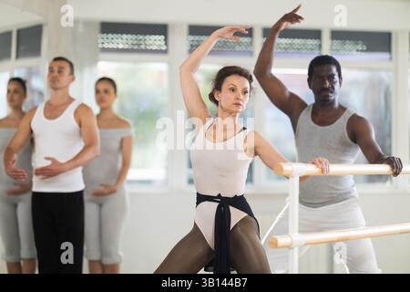 Female ballet instructor practicing demi plie at barre with students Stock Photo