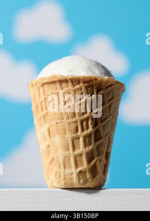 vanilla ice cream in waffle cone on blue sky background Stock Photo