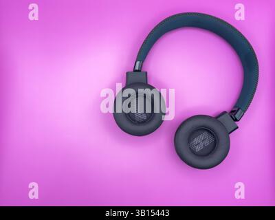 Green headphones with soft inverted earbuds with the letters L and R and a soft headband are lying on the right side of the image on a pink background Stock Photo