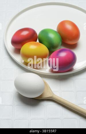 Coloured eggs on a plate and uncoloured eggs on a spoon, Easter celebration Stock Photo