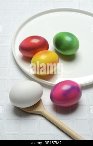 Coloured eggs on a plate and uncoloured eggs on a spoon, Easter celebration Stock Photo