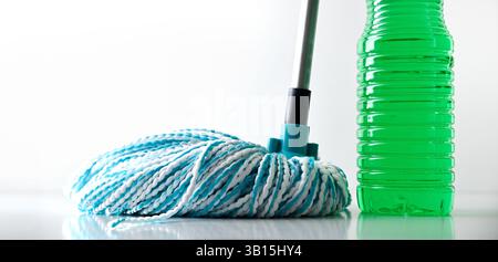 Plastic bottle with green disinfectant product for floor and mop with white and blue fiber strips on reflective floor and white isolated background. F Stock Photo