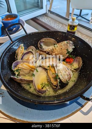 A delicious pan of freshly cooked clams served on a blue plate, ready to be enjoyed. The dish is accompanied by a small bowl of tomato sauce. Stock Photo