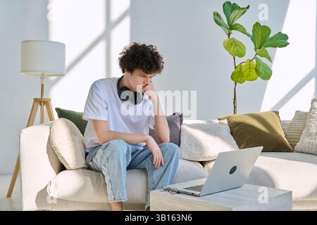 Young handsome serious guy looking at laptop screen sitting on sofa at home Stock Photo