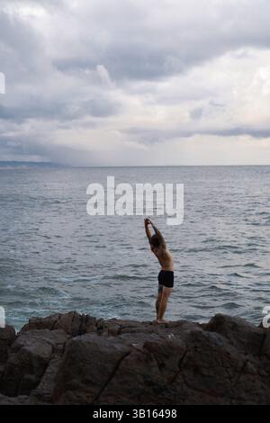 Man doing yoga on a rock by the ocean Stock Photo