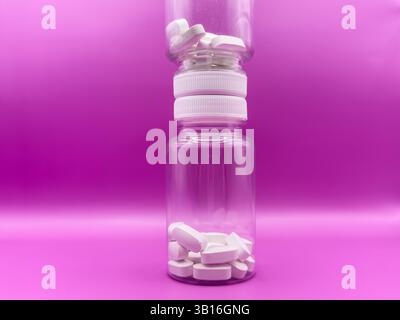 Two transparent jars with white pills, one jar stands on top of the other in the form of a tower, on a pink background, front view. High quality photo Stock Photo