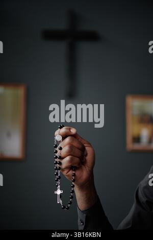Vertical shot of unrecognizable male hand holding black rosary with silver cross Stock Photo