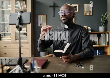 Young African American priest gesticulating in air while having online bible study in office Stock Photo