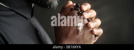 Website banner of unrecognizable pastor holding beautiful rosary with silver cross while praying Stock Photo