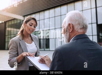 Senior business man and young business woman discussing a document outdoors on a sunny day Stock Photo