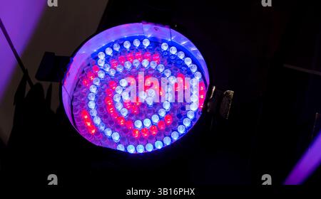 Closeup of one colorful stage spotlight with red, blue, purple LED bulbs in a spiral pattern, single spot light glowing in dark room, professional sta Stock Photo