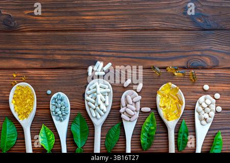Assorted Supplements on Wooden Spoons. A variety of dietary supplements arranged on wooden spoons with green leaves on a rustic wooden background. Stock Photo