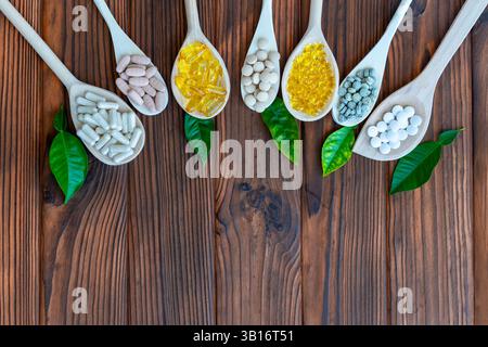 Variety of supplements on wooden spoons with green leaves. Wooden spoons are arranged in a row, each filled with different types of supplements. Top Stock Photo