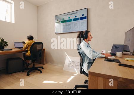 Female workers in a bright professional office, focused on computers with a project board visible. Stock Photo