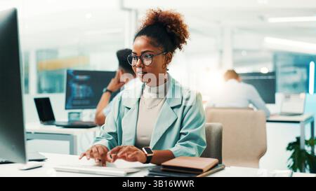 Programmer, woman and typing on computer in office for software development, code debugging and testing app. African person, employee and technology Stock Photo