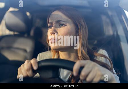 Close up of a worried young woman in drivers seat standing in traffic jam with her hands on steering wheel Stock Photo
