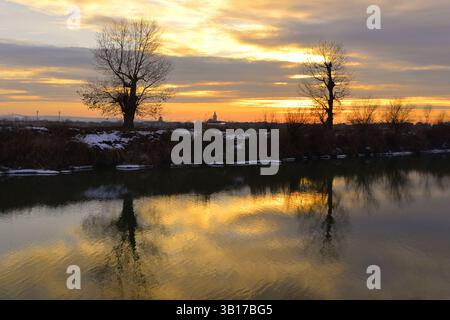 Sunset over the Mures river with the silhouettes of the trees reflected in the water Stock Photo