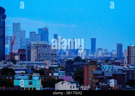 The London skyline at dusk, with the silhouettes of skyscrapers and construction cranes against a deep blue sky. Stock Photo