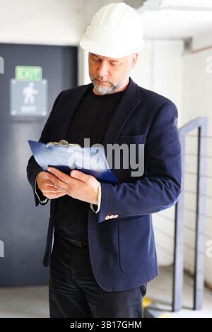 Engineer with blue folder on construction site, wearing helmet and smart casual outfit. Stock Photo