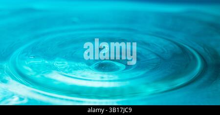 Water droplets fall down closely into the blue water, making it the perfect center in nature Stock Photo
