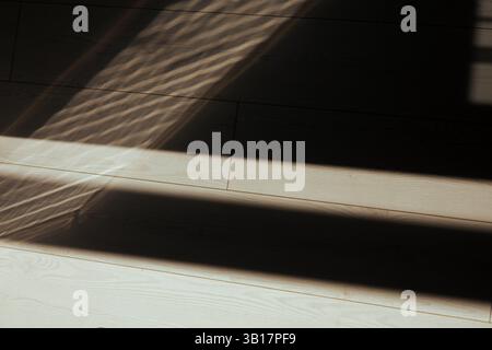 Sunlight creates geometric shadows on a wooden floor, forming abstract pattern. Abstract image showing wooden floor and shadows from window or blinds. Stock Photo