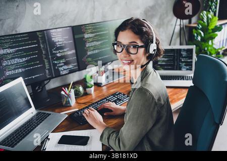 Young female software developer working remotely on a programming project, smiling confidently in a modern home office environment Stock Photo