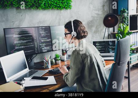 Young female programmer working at office desk with multiple screens, wearing casual attire, focused on coding and programming Stock Photo