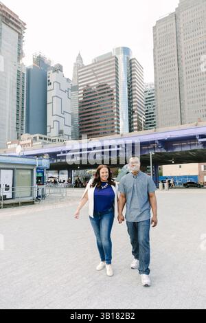 Couple walks hand in hand through urban area surrounded by skyscrapers during daylight Stock Photo