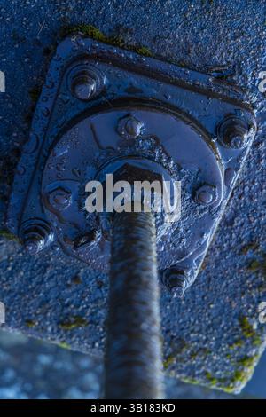 Large wet screw with bolts and nuts fixing a metal plate to concrete surface Stock Photo