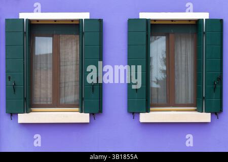 Two green shuttered windows on purple wall Stock Photo