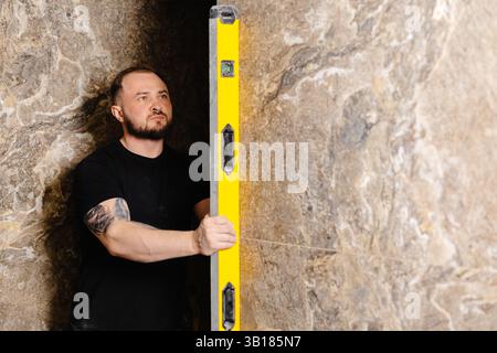 Builder checking the evenness of marble tiles with a level tool, ensuring precision and accuracy during renovation work on a wall Stock Photo
