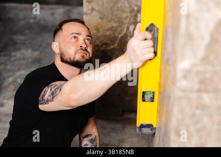 Builder checking the evenness of marble tiles with a level tool, ensuring precision and accuracy during renovation work on a wall Stock Photo