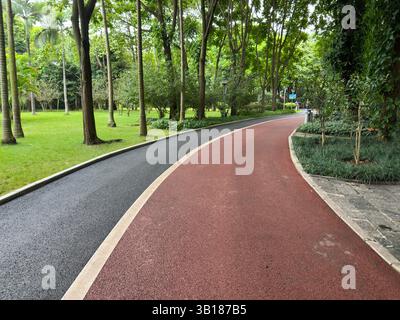 View of a red path winding through a lush green park under the sunlight in China. Stock Photo