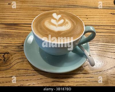 Creamy latte with heart-shaped art sits on a wooden table, ready to be enjoyed as a morning treat. Stock Photo