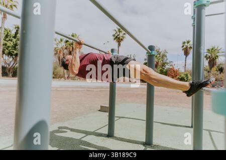 A strong man is doing Australian pull ups at a calisthenics outdoor gym in a tropical location. Stock Photo