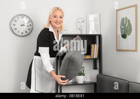 Middle-aged chambermaid adjusting pillows on sofa in hotel room Stock Photo