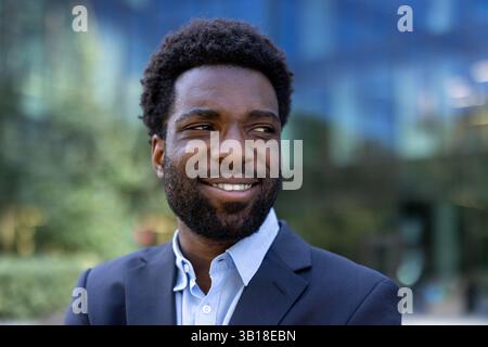 Successful African American businessman outside office building, smiling happily to the side. Man in business suit close-up. Stock Photo
