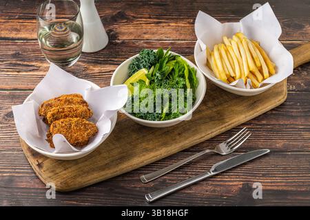 Crispy chicken wings with greens and french fries on wooden table Stock Photo