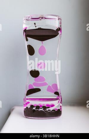 A liquid purple motion timer with pink and black liquid flowing, creating a visually pleasing and relaxing display. Vertical shot. Stock Photo