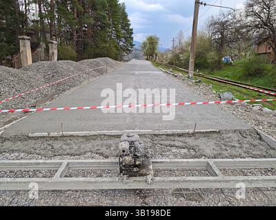 Construction workers building a new concrete road next to railroad tracks, using a concrete vibrator Stock Photo
