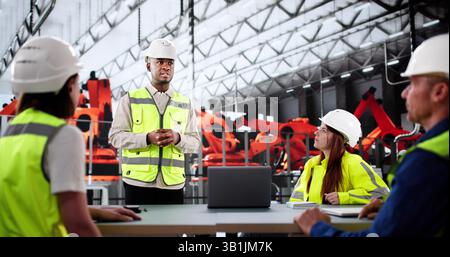 Multiethnic Team Of Engineers Discussing Production On Factory Assembly Line. Stock Photo