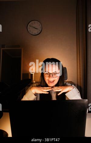 Millennial woman celebrating victory in home office, businesswoman working with laptop joyfully holding hands up, satisfied received excellent results Stock Photo